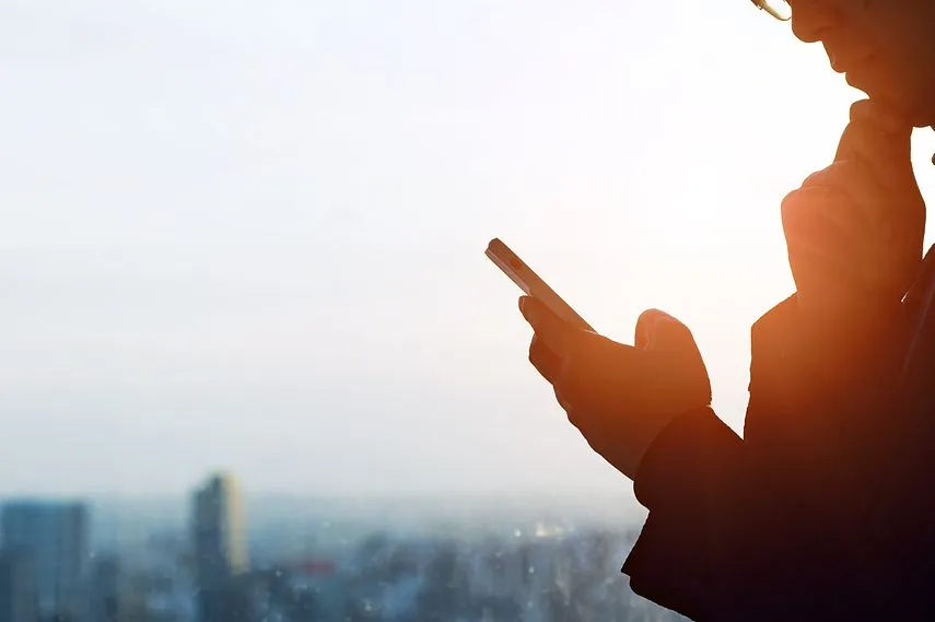 Silhouette of a man thinking while looking at his smartphone.