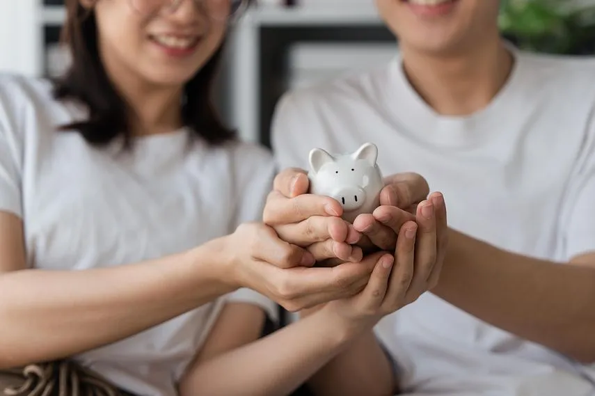 Happy asian young couple love calculate and putting coin in piggy bank for saving money to buy real estate for new home. Business finance, deposit with banking for financial planning future together