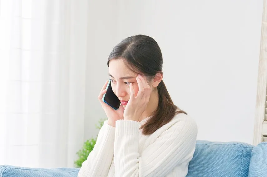 リビングで悩みながらスマホで電話する女性
