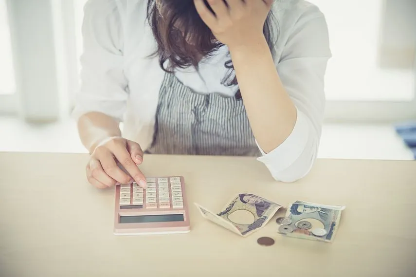 女性が部屋で電卓とお金を出して頭を抱えている　woman money