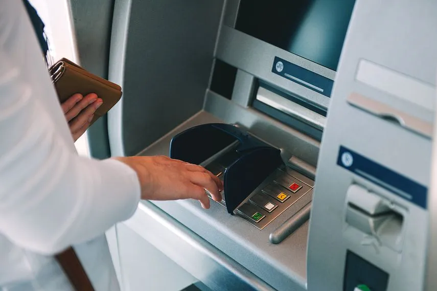 Woman using ATM holding wallet an pressing the PIN security number on the keyboard automatic teller machine