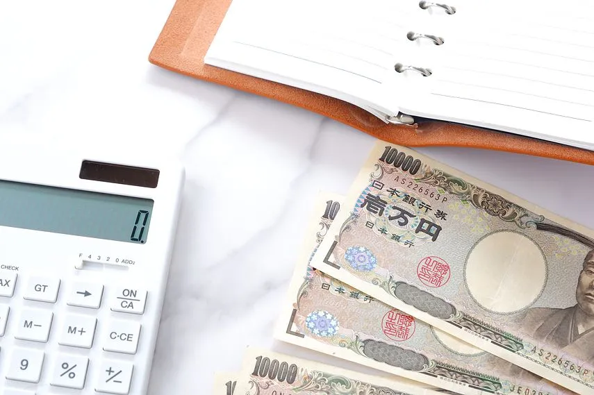 机の上に開いておかれたリング式のシステム手帳、電卓、福沢諭吉の肖像の一万円札紙幣