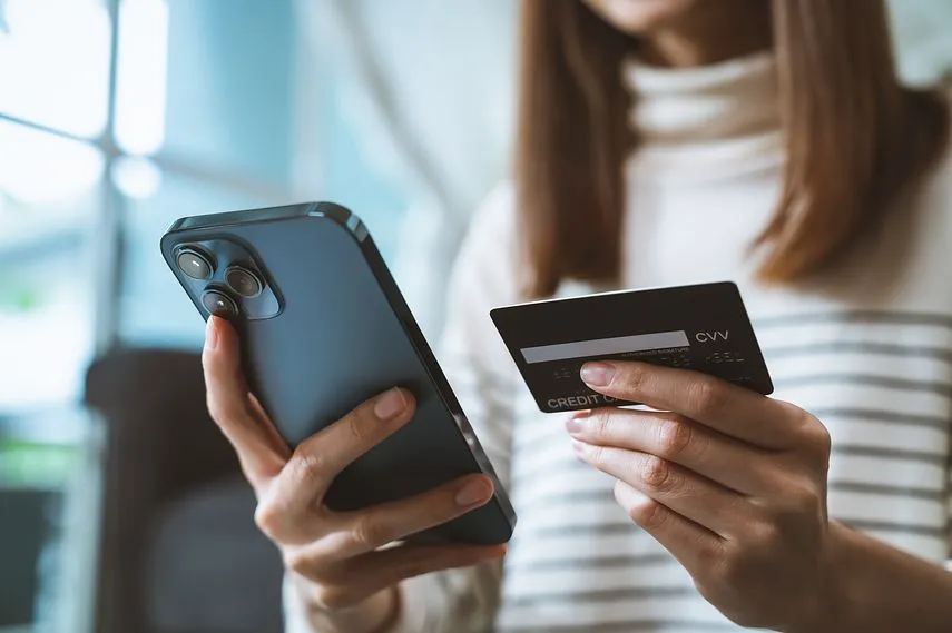 クレジットカードを持ち、スマートフォンを使ってインターネットバンキングで支払いをしてオンラインショッピングをする女性の手。