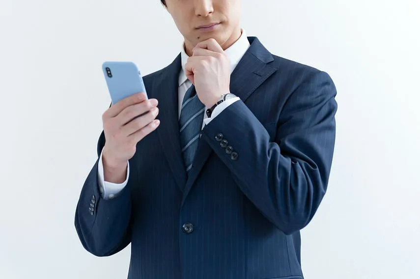 携帯を持ち悩むスーツを着た日本人男性