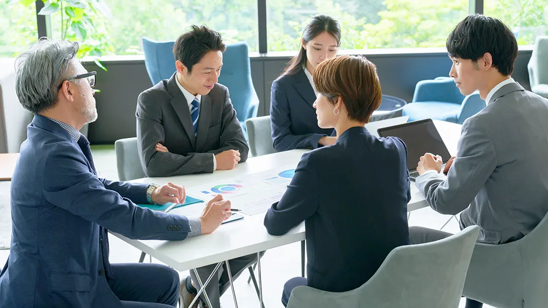 会議机を挟み話している様子の5名