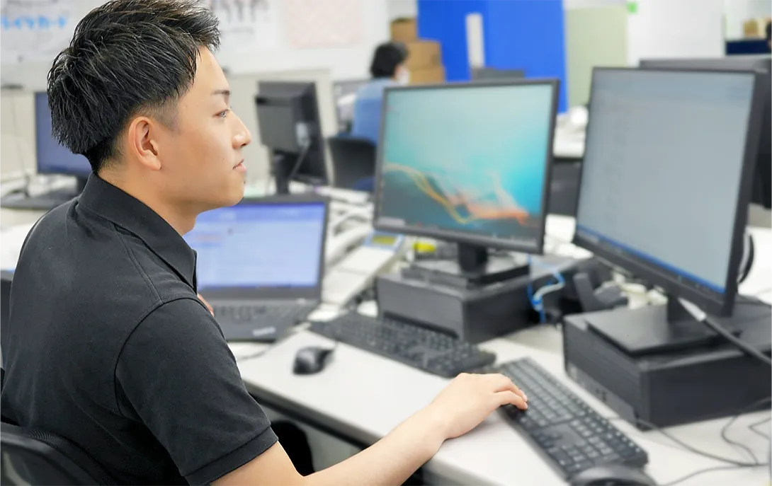 パソコンが複数並んでいるうちの一つのモニターを見る社員