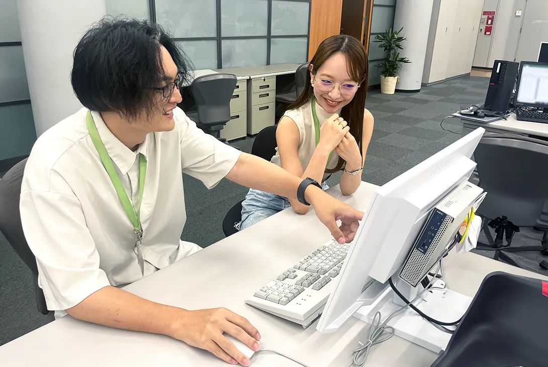 1つのモニターを指さしながら和やかな雰囲気でディスカッションをしている二人