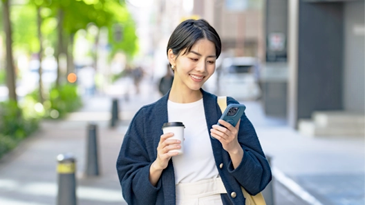 外でスマホとコーヒーを持ちプライベートを楽しむ様子